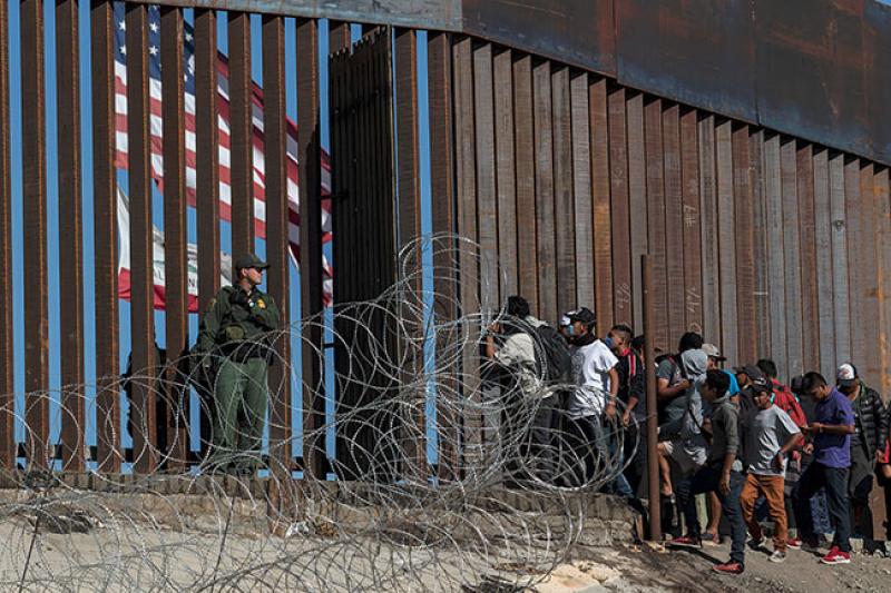 Des migrants d’Amérique centrale regardent à travers la clôture surveillée par les gardes-frontières américains. Près du poste frontalier d’El Chaparral, Tijuana, État de Basse-Californie, Mexique, 25 novembre 2018. © Guillermo Arias / AFP.