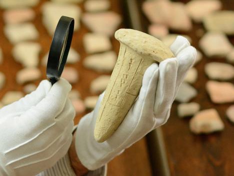 Archéologue observant un clou orné d'écritures cunéiformes à la loupe. © Santabiblia, 2015, CC BY-SA 4.0