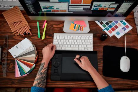 Vue de dessus d'un graphiste professionnel utilisant une tablette graphique, un ordinateur et des nuanciers à son poste de travail. © Svitlana / AdobeStock / droits by Rocket Links